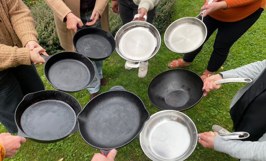 A group of people standing in a circle, holding stainless steel and cast iron pans.